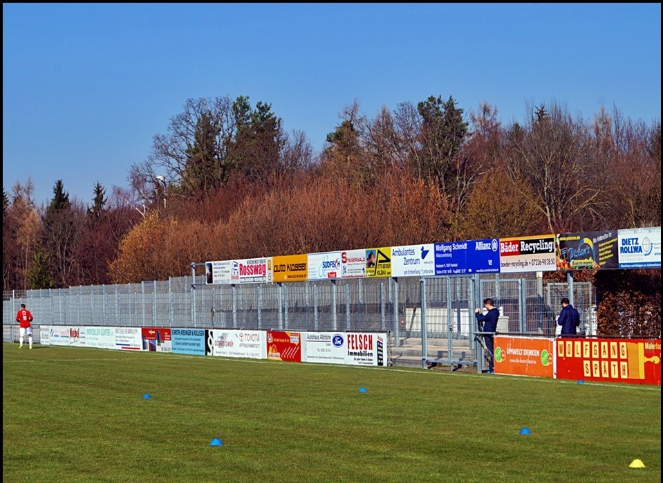 Gästetribüne mit mehreren Werbebannern am Spielfeldrand
